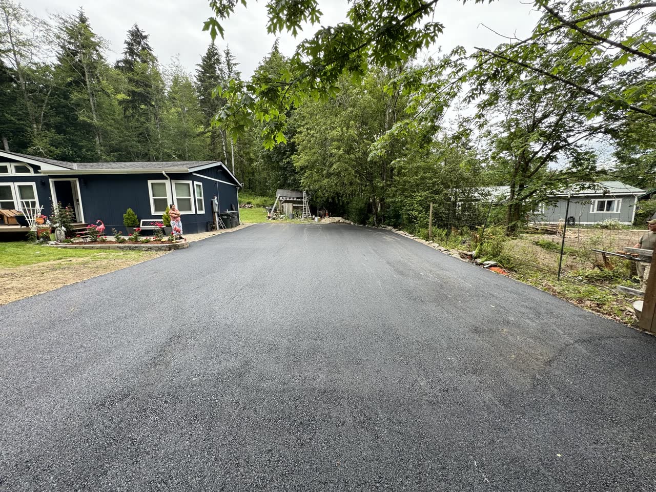 Asphalt driveway past a barn under blue sky
